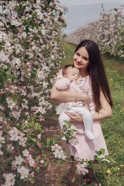 Mãe e sua filhinha perto das árvores floridas. Mãe nova e bebê no jardim. Flor pomar de maçã. — Fotografia de Stock