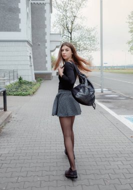 Deri sırt çantalı, ceketli kadın sabah ya da akşam şehir sokağına çıkıyor. Güneş ışınları parlıyor. Sıradan kış kıyafetlerinin ayrıntıları..