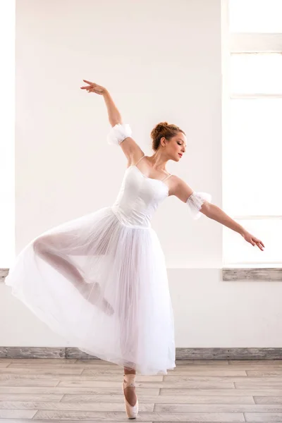 Young graceful ballerina dancing on white studio.