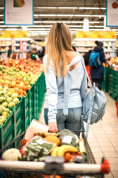 Woman pulls full trolley at the supermarket.