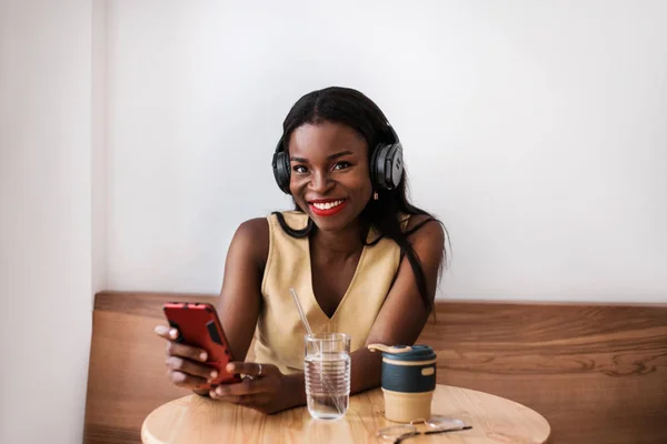 Smiling black girl listening to music on smartphone at cafe.