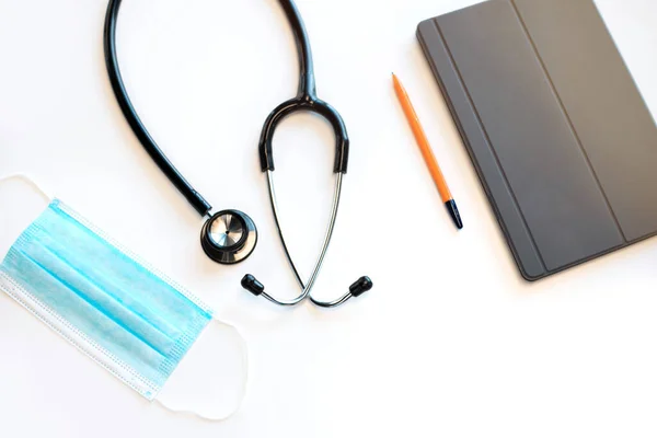 Doctor\'s table at medical clinic. Stethoscope, mask and digital tablet are on the table.