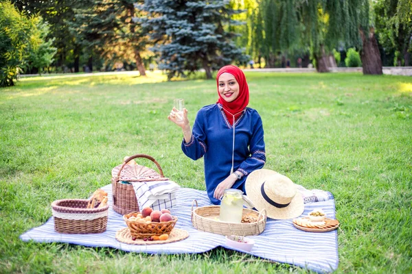 Beautiful Muslim woman on picnic at sunny day holding straw hat and smiling.