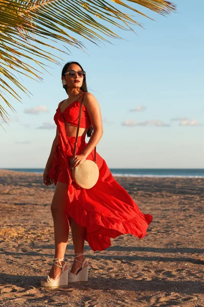 Güzel kırmızı elbisesiyle sahilde poz veren zarif, beyaz bir kadın model.