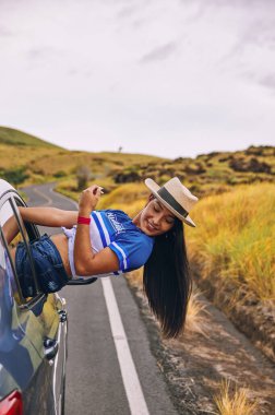 Arabanın camında oturmuş şapkasını takmış mutlu bir genç kadın seyahatin tadını çıkarıyor ve eğleniyor.