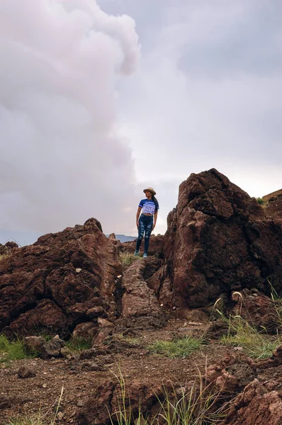Yanardağ kraterinin yanındaki volkanik kayanın üzerinde duran şapkalı bir kadın, Masaya volkanı ulusal parkında.