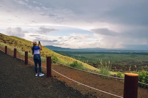Volkan Ulusal Parkı 'nda akıllı telefonla manzara fotoğrafları çeken genç bir kadın.