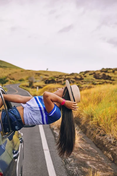 Arabanın camında oturmuş şapkasını takmış mutlu bir genç kadın seyahatin tadını çıkarıyor ve eğleniyor.