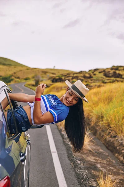 Arabanın camında oturmuş şapkasını takmış mutlu bir genç kadın seyahatin tadını çıkarıyor ve eğleniyor.