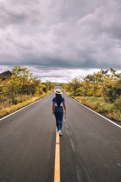 Elinde şapkasıyla gezen bir kadın volkan ulusal parkında sessiz bir yolun ortasında yürüyor.