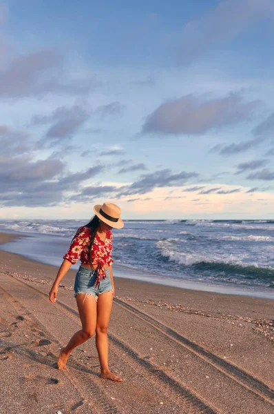 Gün batımında sahilde yürüyen genç bir kadın.