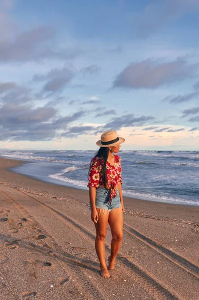 Sahilde yürüyen genç bir kadın gün batımında ufka bakıyor..
