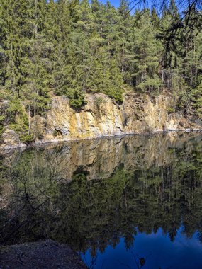 Ağaçlar ve kayalar durgun su yüzeyine yansıyor.