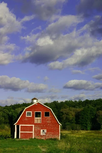 Canlı bir kırmızı ahır, bir yatak yeşil çim ve süpürme mavi gökyüzü ile güzel bir gün.