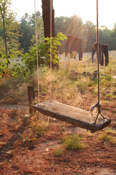 Bir kamp bir ağaçtan asılı ahşap ve halat bir tahta yapılmış eski bir moda salıncak. Çamaşırhane arka planda hat üzerinde kurutma görülebilir.