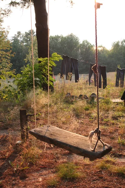 Bir kamp bir ağaçtan asılı ahşap ve halat bir tahta yapılmış eski bir moda salıncak. Çamaşırhane arka planda hat üzerinde kurutma görülebilir.