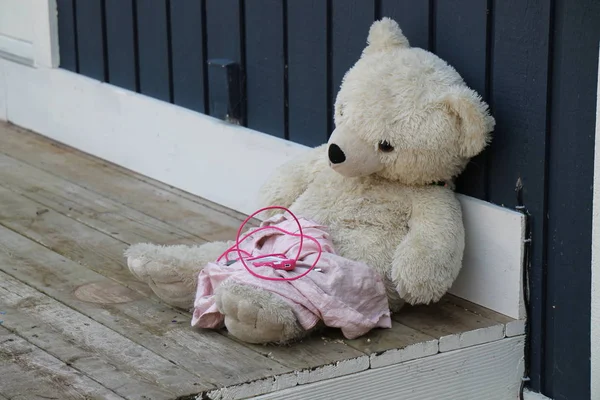  Bir kirli beyaz oyuncak ayı verandada kirli küçük pembe battaniye ve cep telefonu ile eğiliyor.