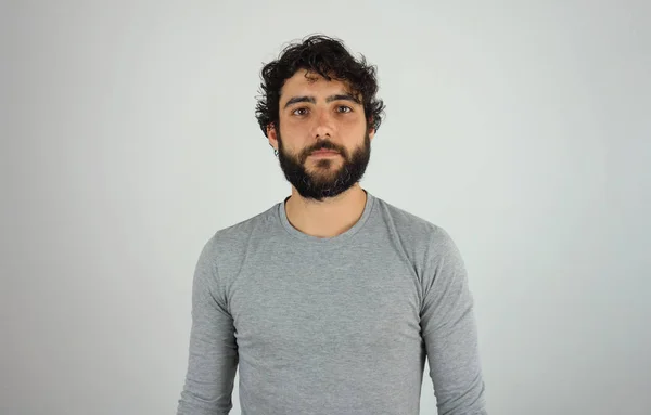 Handsome brunette man with beard and curly hair studio portrait over gray background.