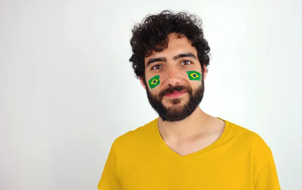 Sport fan smiling looking at camera. Man with the flag of Brazil makeup on his face and yellow t-shirt.