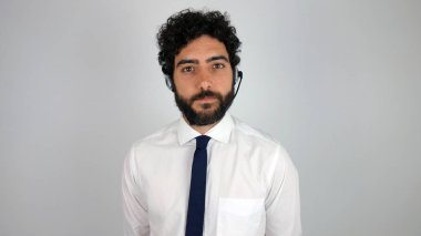 Çağrı merkezi gri arka plan üzerinde kulaklık, yakışıklı danışman. Genç ve esmer adam kameraya ciddi bakan.
