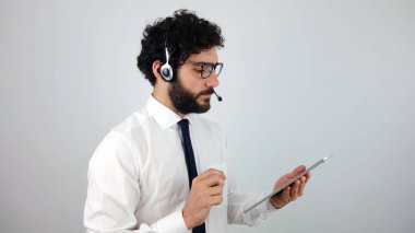 Çağrı merkezi ile bir tablet gri arka plan üzerinde kulaklık, yakışıklı danışman. Genç ve esmer adam al tablet arıyor.