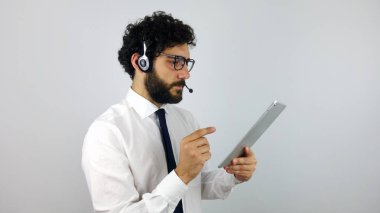 Çağrı merkezi ile bir tablet gri arka plan üzerinde kulaklık, yakışıklı danışman. Genç ve esmer adam al tablet arıyor.
