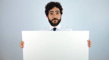 Yakışıklı adam yüzünde boş bir afiş ile kopya alanı metin veya reklam, gri bir arka plan üzerinde tutarak gülümseyen bir ifade ile