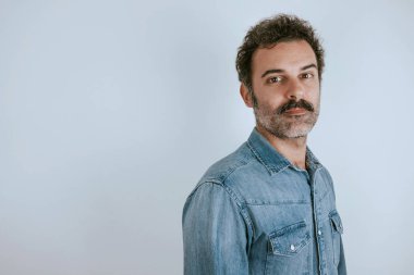 Kameraya bakarak kot gömlek ayakta bıyıklı kahverengi, yakışıklı adam portresi. Gri arka planı.