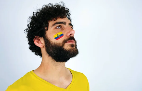 Sport fan head high and feeling proud when listening to the anthem of his country. Man with the flag of Ecuador makeup on his face and yellow t-shirt.