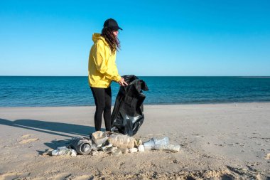 Çöp ve plastik toplayan kadın çöp torbasıyla plajı temizliyor. İklim değişikliği ve okyanusların kirliliğine karşı çevre gönüllü aktivisti.