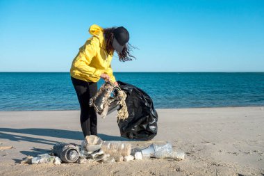 Çöp ve plastik toplayan kadın çöp torbasıyla plajı temizliyor. İklim değişikliği ve okyanusların kirliliğine karşı çevre gönüllü aktivisti.