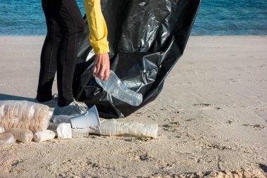 Çöp ve plastik toplayan kadın çöp torbasıyla plajı temizliyor. İklim değişikliği ve okyanusların kirliliğine karşı çevre gönüllü aktivisti.