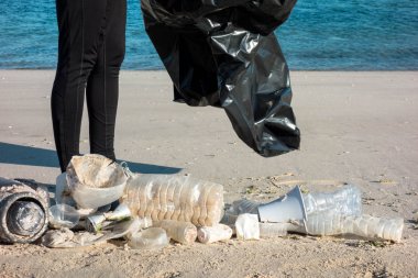 Çöp ve plastik toplayan kadın çöp torbasıyla plajı temizliyor. İklim değişikliği ve okyanusların kirliliğine karşı çevre gönüllü aktivisti.