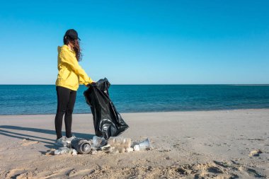 Çöp ve plastik toplayan kadın çöp torbasıyla plajı temizliyor. İklim değişikliği ve okyanusların kirliliğine karşı çevre gönüllü aktivisti.