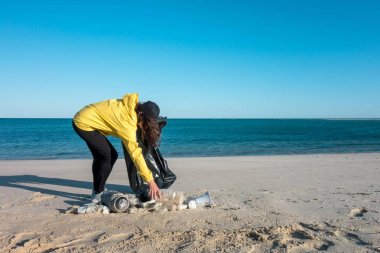Çöp ve plastik toplayan kadın çöp torbasıyla plajı temizliyor. İklim değişikliği ve okyanusların kirliliğine karşı çevre gönüllü aktivisti.
