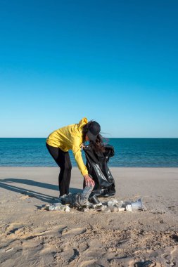Çöp ve plastik toplayan kadın çöp torbasıyla plajı temizliyor. İklim değişikliği ve okyanusların kirliliğine karşı çevre gönüllü aktivisti.