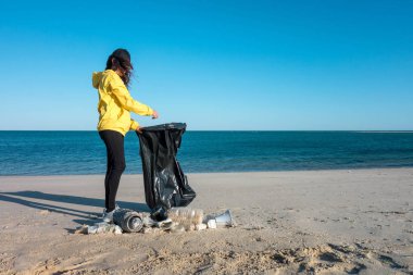 Çöp ve plastik toplayan kadın çöp torbasıyla plajı temizliyor. İklim değişikliği ve okyanusların kirliliğine karşı çevre gönüllü aktivisti.