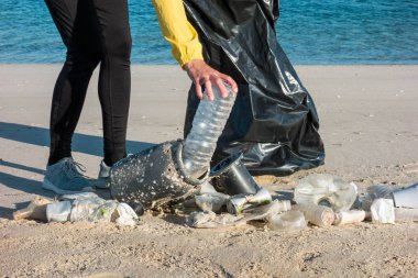Çöp ve plastik toplayan kadın çöp torbasıyla plajı temizliyor. İklim değişikliği ve okyanusların kirliliğine karşı çevre gönüllü aktivisti.