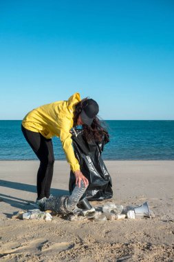 Çöp ve plastik toplayan kadın çöp torbasıyla plajı temizliyor. İklim değişikliği ve okyanusların kirliliğine karşı çevre gönüllü aktivisti.