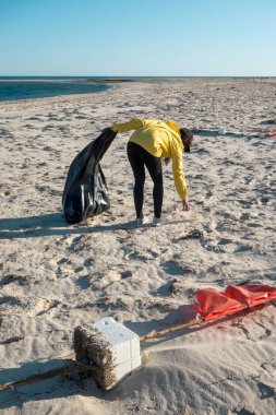 Çöp ve plastik toplayan kadın çöp torbasıyla plajı temizliyor. İklim değişikliği ve okyanusların kirliliğine karşı çevre gönüllü aktivisti.