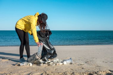 Çöp ve plastik toplayan kadın çöp torbasıyla plajı temizliyor. İklim değişikliği ve okyanusların kirliliğine karşı çevre gönüllü aktivisti.