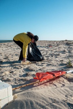 Çöp ve plastik toplayan kadın çöp torbasıyla plajı temizliyor. İklim değişikliği ve okyanusların kirliliğine karşı çevre gönüllü aktivisti.