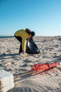 Çöp ve plastik toplayan kadın çöp torbasıyla plajı temizliyor. İklim değişikliği ve okyanusların kirliliğine karşı çevre gönüllü aktivisti.