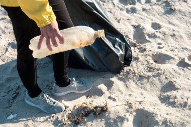 Çöp ve plastik toplayan kadın çöp torbasıyla plajı temizliyor. İklim değişikliği ve okyanusların kirliliğine karşı çevre gönüllü aktivisti.