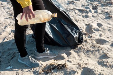 Çöp ve plastik toplayan kadın çöp torbasıyla plajı temizliyor. İklim değişikliği ve okyanusların kirliliğine karşı çevre gönüllü aktivisti.