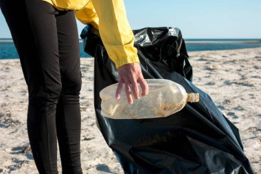 Çöp ve plastik toplayan kadın çöp torbasıyla plajı temizliyor. İklim değişikliği ve okyanusların kirliliğine karşı çevre gönüllü aktivisti.