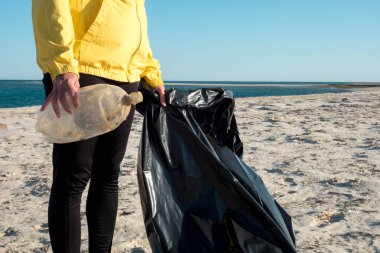 Çöp ve plastik toplayan kadın çöp torbasıyla plajı temizliyor. İklim değişikliği ve okyanusların kirliliğine karşı çevre gönüllü aktivisti.