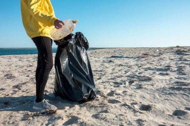Çöp ve plastik toplayan kadın çöp torbasıyla plajı temizliyor. İklim değişikliği ve okyanusların kirliliğine karşı çevre gönüllü aktivisti.