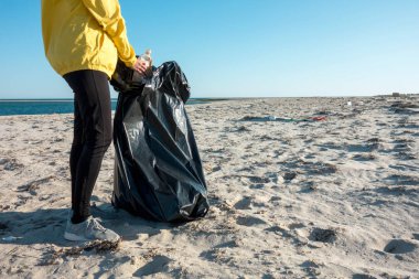 Çöp ve plastik toplayan kadın çöp torbasıyla plajı temizliyor. İklim değişikliği ve okyanusların kirliliğine karşı çevre gönüllü aktivisti.