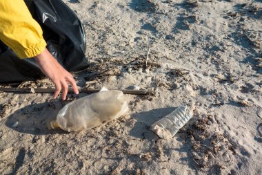 Çöp ve plastik toplayan kadın çöp torbasıyla plajı temizliyor. İklim değişikliği ve okyanusların kirliliğine karşı çevre gönüllü aktivisti.